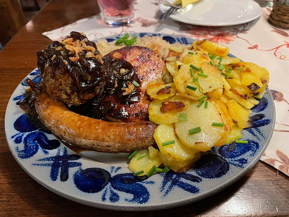 Pfälzer Teller — Bratwurst, Leberknödel und Saumagen mit Bratkartoffeln und Sauerkraut auf blauem Zwiebelmuster-Geschirr