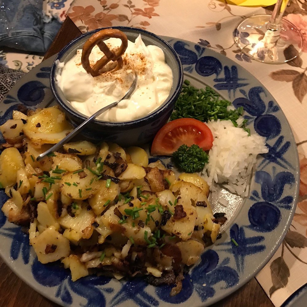 Weißer Käse mit Bratkartoffeln und Brezel auf blauem Zwiebelmuster-Geschirr